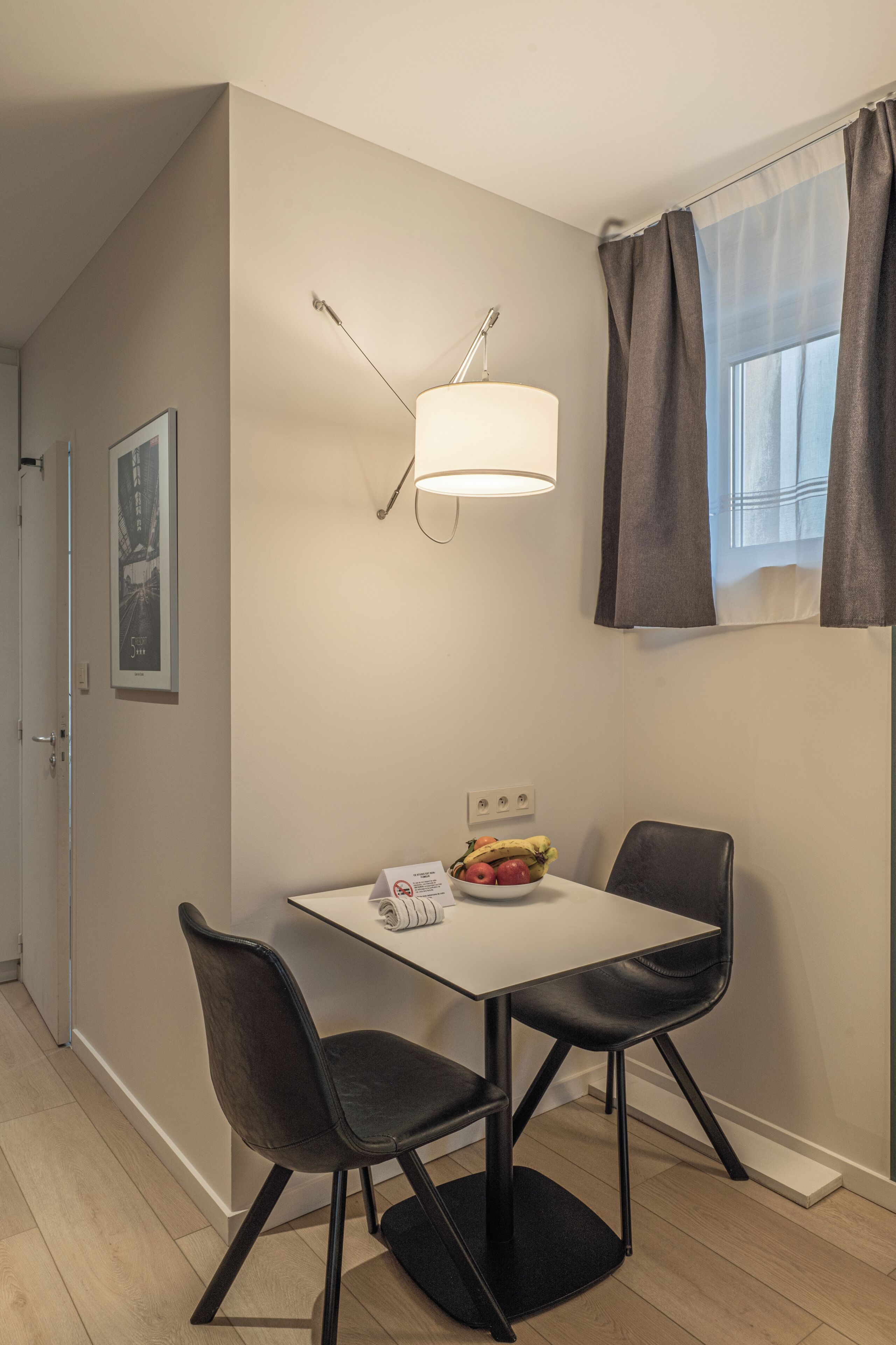 A small dining area with a table, two chairs, a lamp, and a fruit bowl.