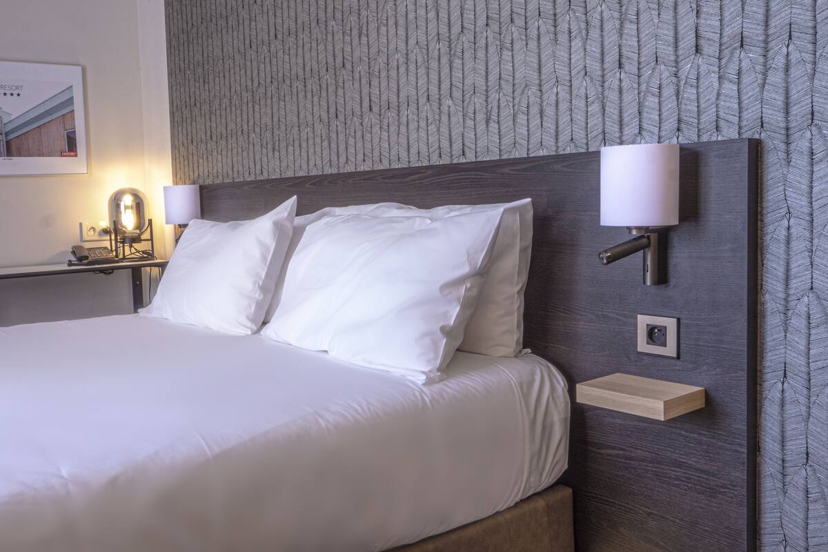 Une chambre d’hôtel avec un grand lit, deux lampes de chevet, une table de chevet avec une lampe et un tableau encadré au mur.