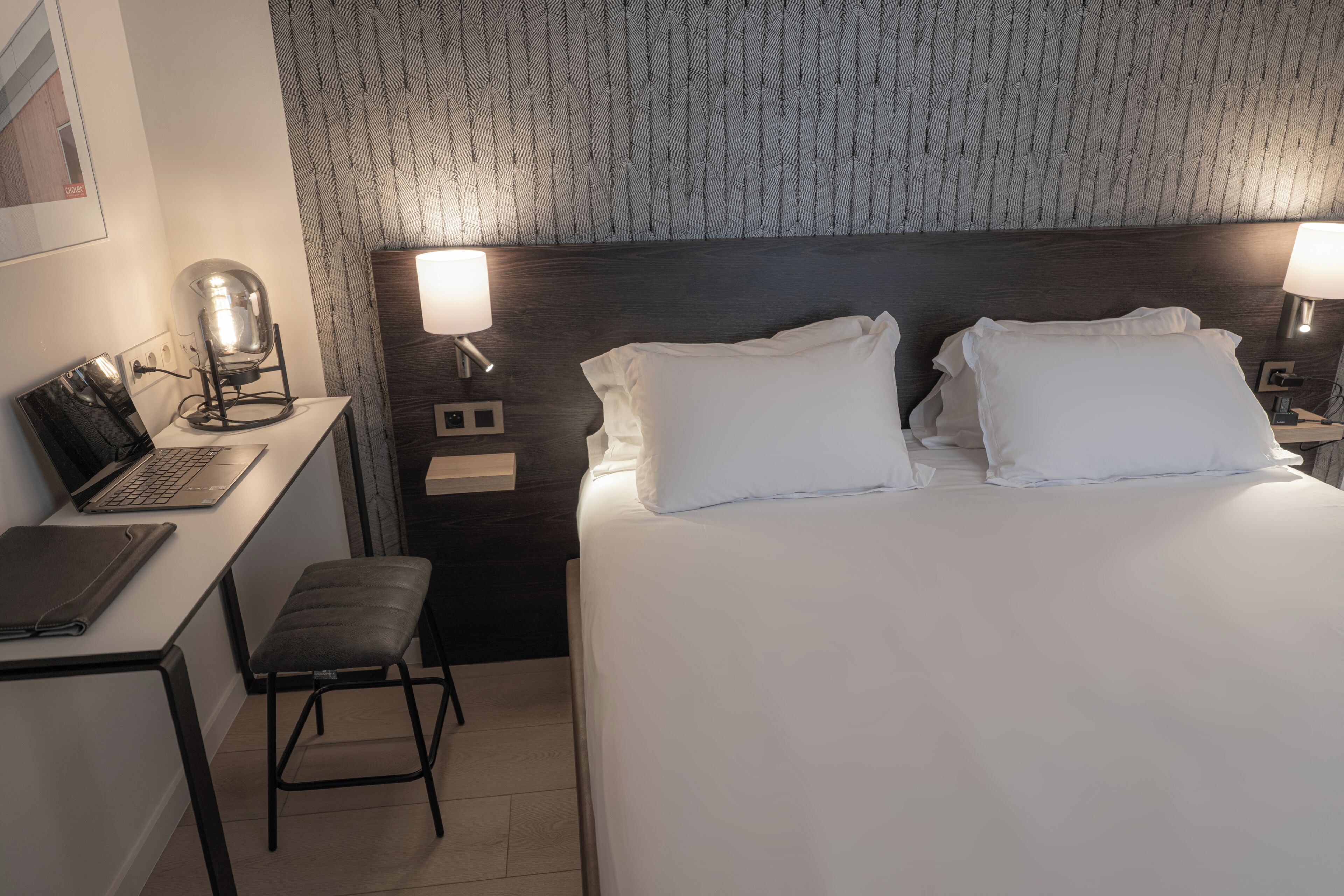 A hotel room with a bed, desk, chair, and two bedside lamps.