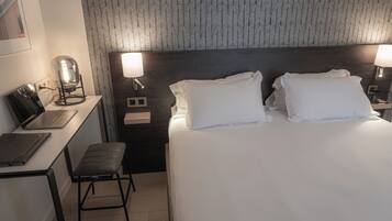 A hotel room with a bed, desk, chair, and two bedside lamps.