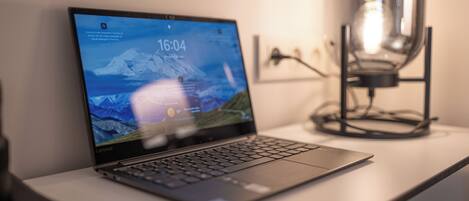 A laptop on a desk with a lamp in the background.