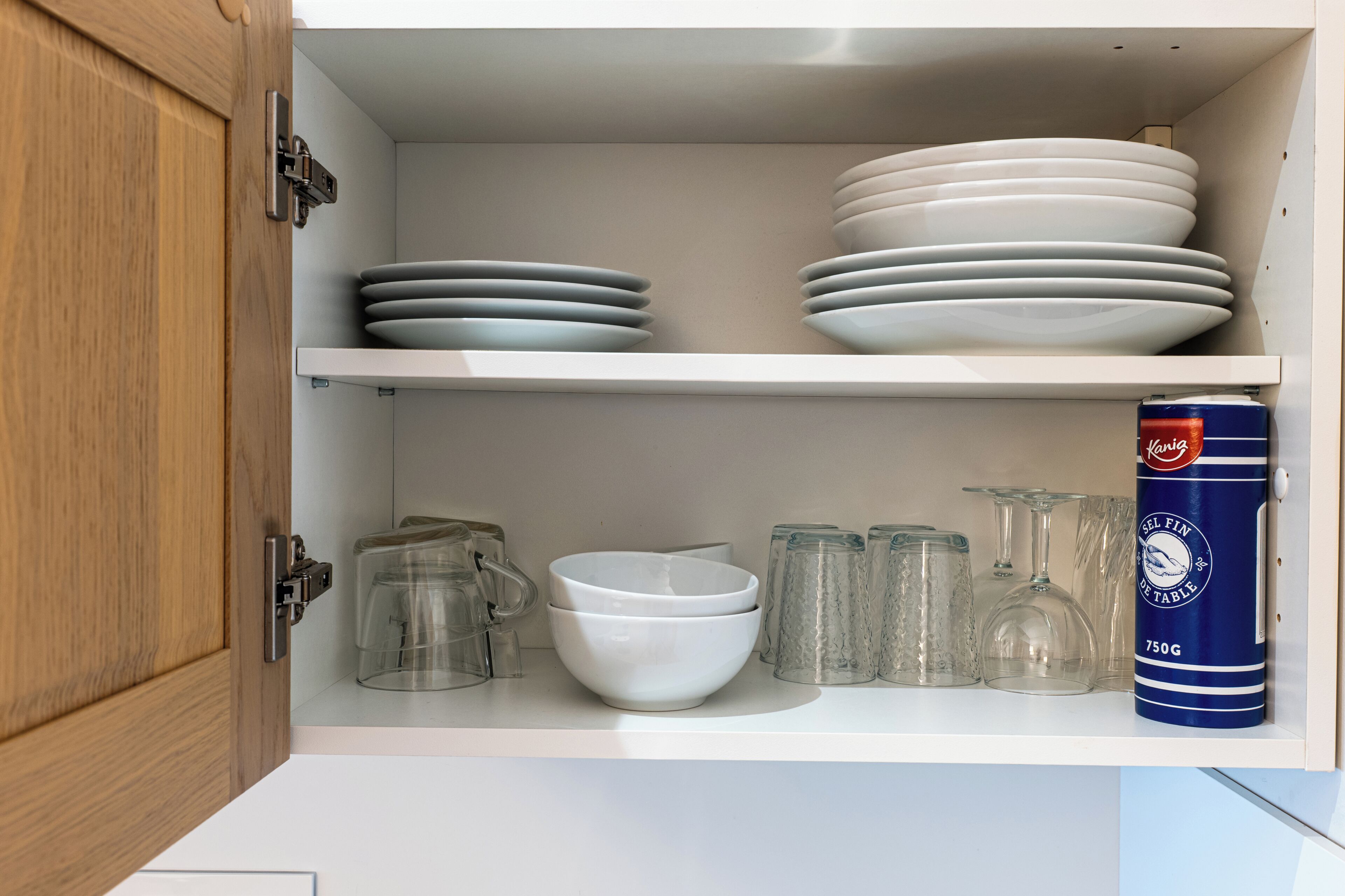 A kitchen cabinet with white and gray plates, a white bowl, and a canister.