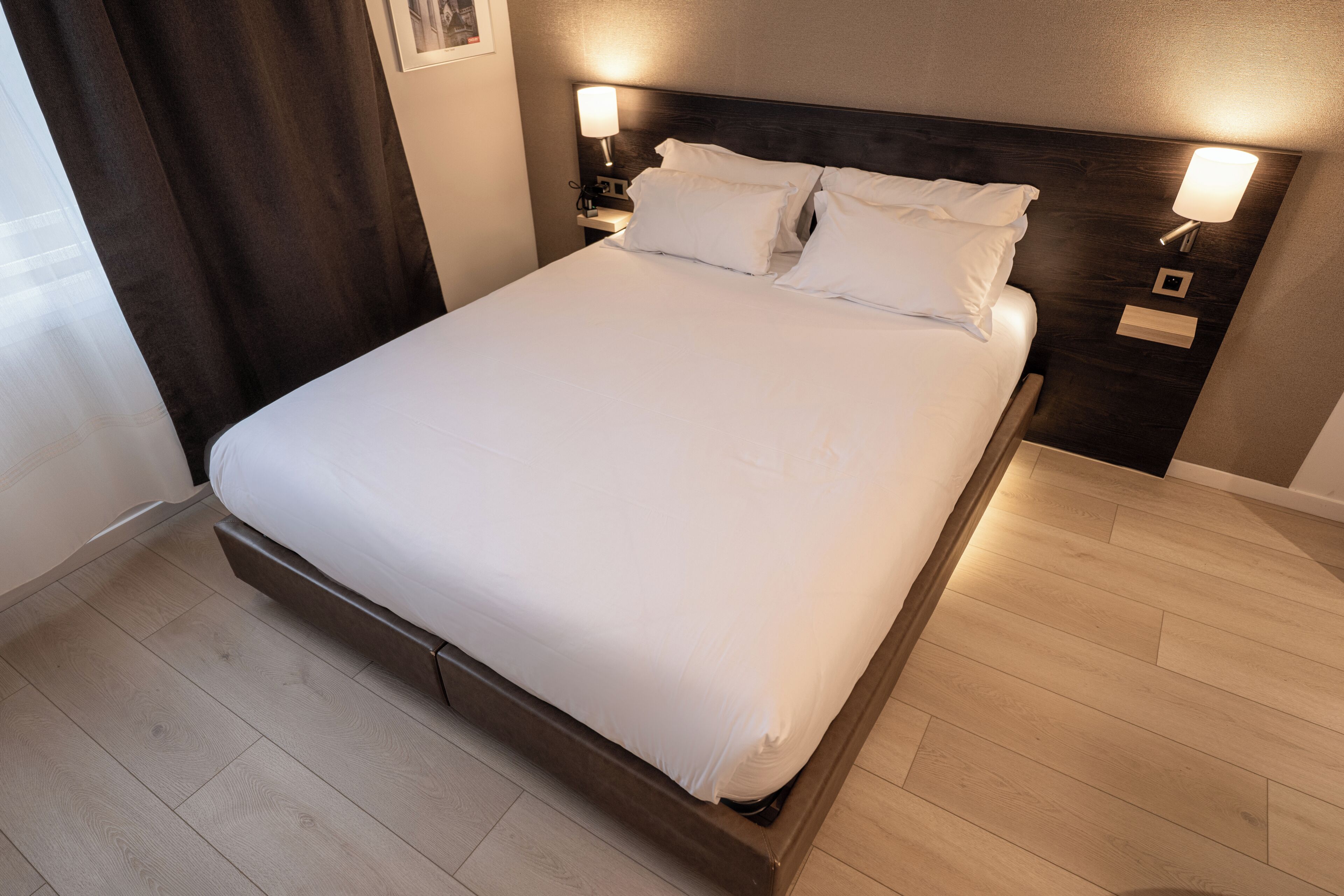 Una cama bien hecha con sábanas blancas, un cabecero oscuro y dos lámparas de noche.