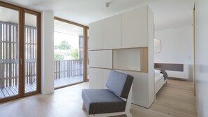 Een moderne, minimalistisch ingerichte kamer met een inbouwed bed, een zithoek en een balkon met houten hekwerk.
