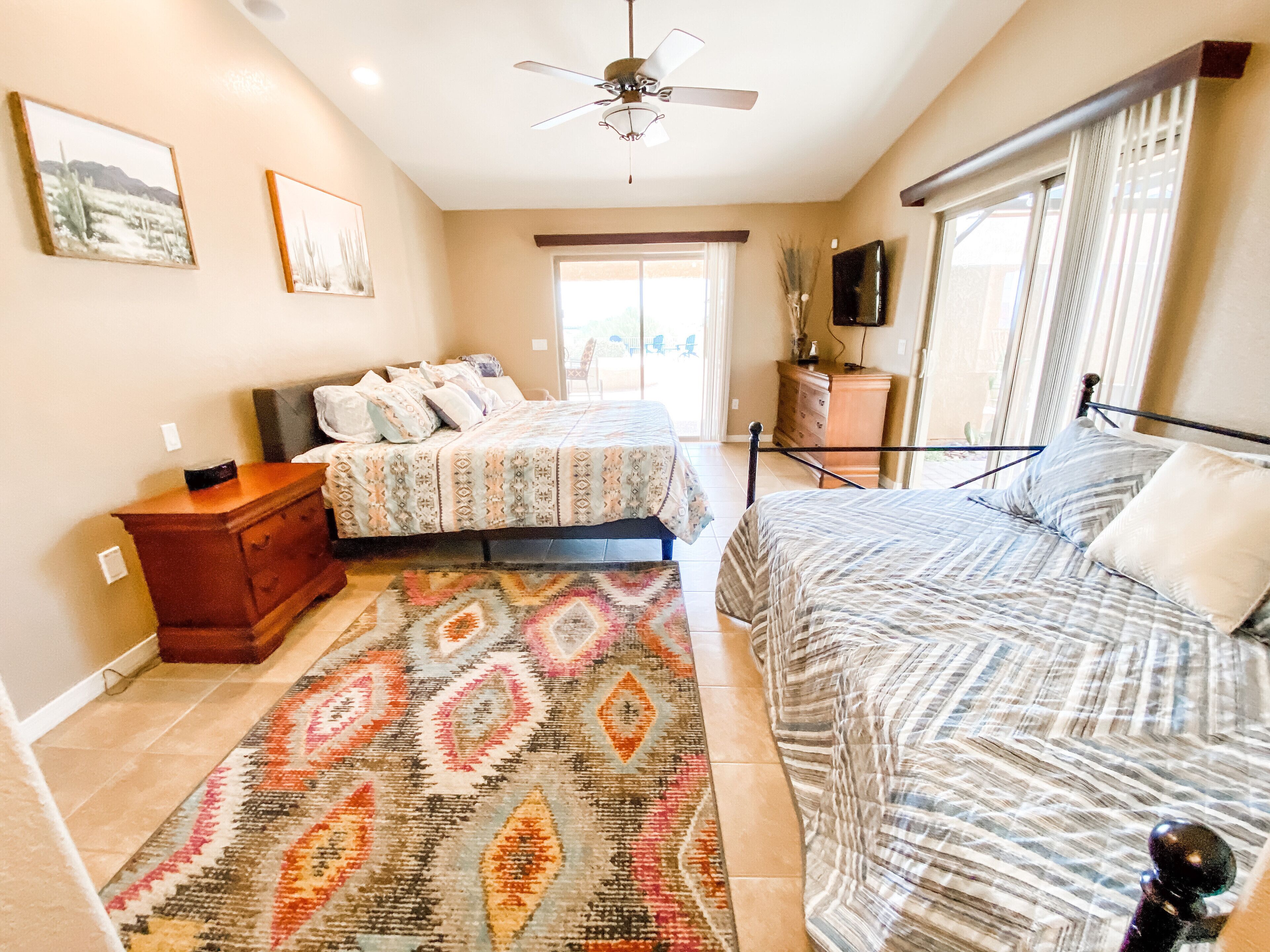 A bedroom with two beds, a ceiling fan, a dresser, and a TV on the wall.