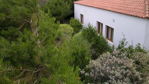 Ein weißes Gebäude mit rotem Ziegeldach, umgeben von üppiger Vegetation und Hügeln im Hintergrund.