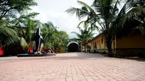 Un sendero pavimentado que lleva a un edificio con una gran entrada arqueada, rodeado de palmeras y una estatua.