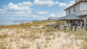 Een strandhuis met een veranda en buitenmeubilair, met uitzicht op het strand en een pier.