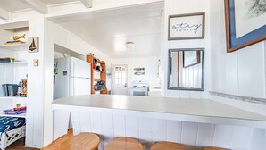 Een keuken met een wit aanrecht, houten krukken en uitzicht op de eetruimte.