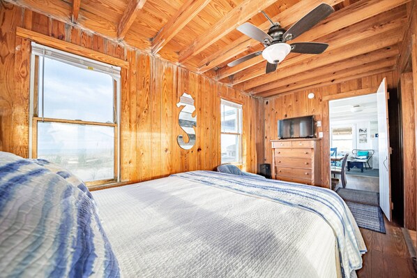 A wooden cabin bedroom with a bed, a ceiling fan, and a TV.
