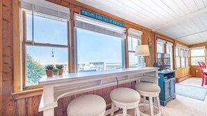 Interior de madeira com área de bar, banquetas, uma televisão e um letreiro que diz “Bem-vindo ao nosso pedaço de paraíso”.