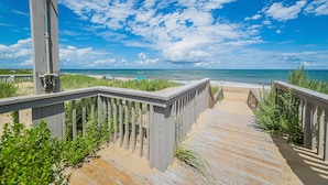 Una passerella di legno che conduce a una spiaggia, con cielo sereno e vista sull'oceano.