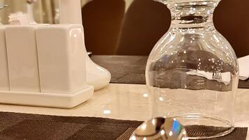Una mesa de comedor dispuesta con un jarrón de vidrio transparente, un jarrón blanco con una flor morada y una cuchara.