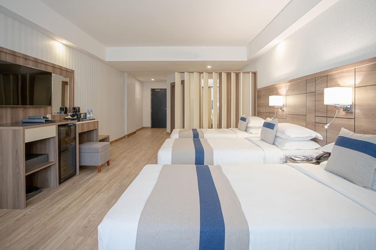 A hotel room with two beds, a desk with a flat-screen TV, a minibar, and a large mirror.