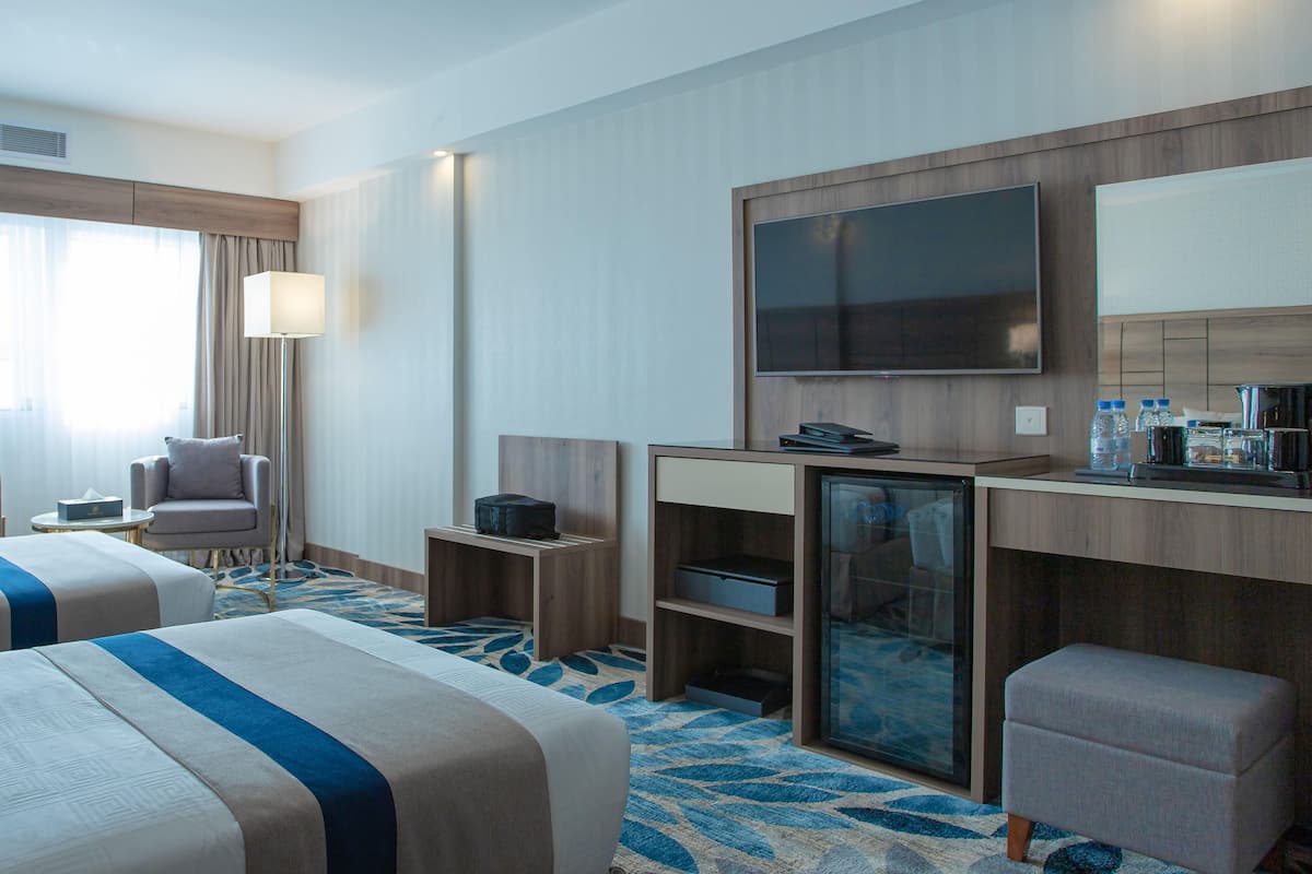 A hotel room with two beds, a desk, a TV, and a minibar.