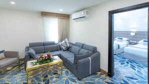 A modern hotel room with a grey sofa, a small table with a flower arrangement, a bed with white bedding, and a blue patterned carpet. - Season Star Hotel (Madinah)