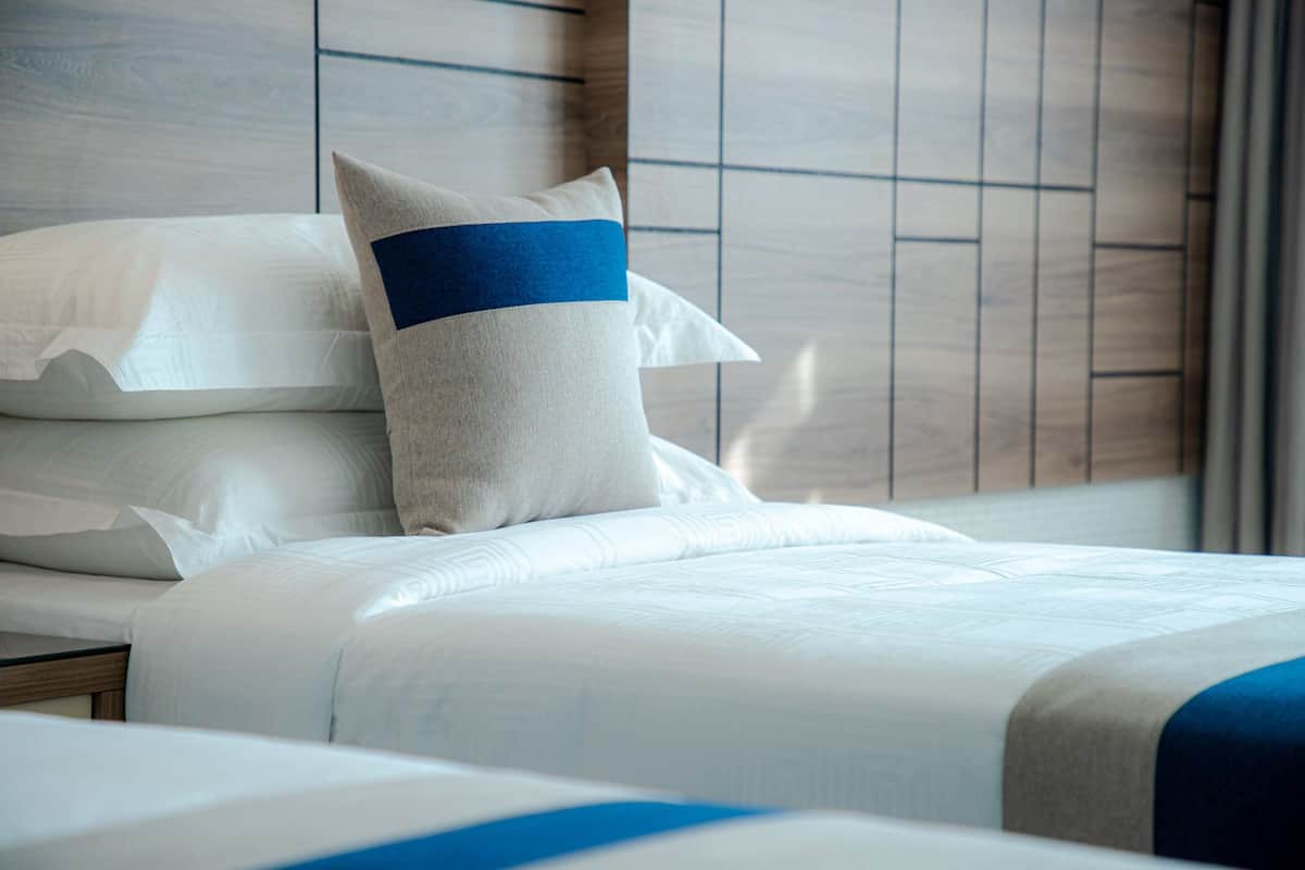 A hotel room with a neatly made bed, a nightstand, and a headboard with a wooden panel design.