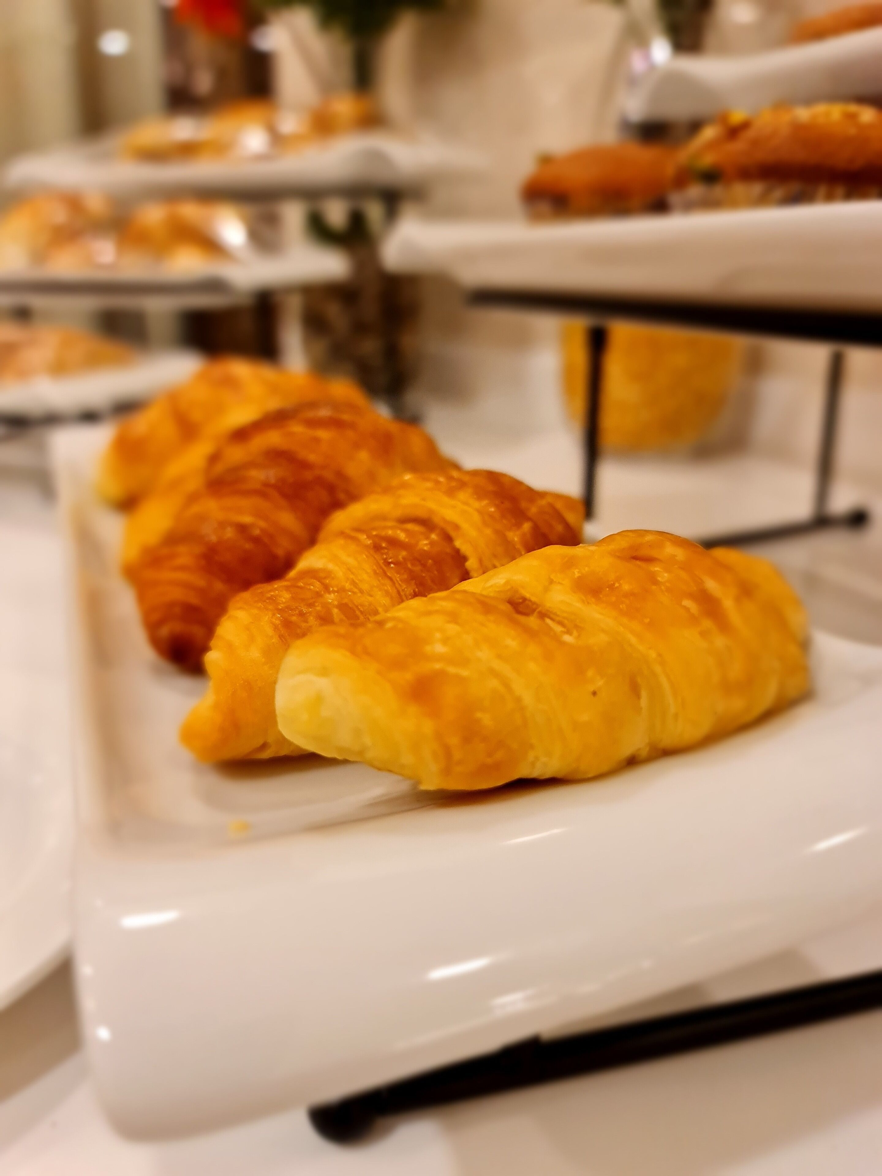 A buffet table with a variety of pastries, including croissants, arranged on white plates.