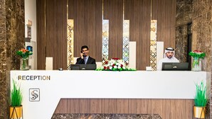 A reception desk with a marble counter, a logo, and two potted plants. - Season Star Hotel (Madinah)