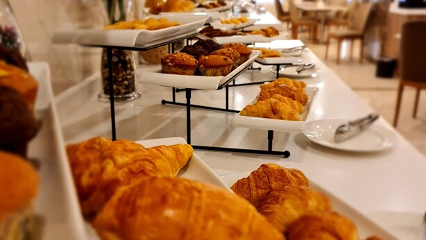 A buffet table with various pastries and baked goods, including croissants and muffins, in a well-lit indoor setting. - Season Star Hotel (Madinah)