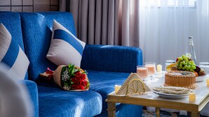 A blue sofa with decorative pillows, a bouquet of red roses, a cake, and a fruit bowl on a table. - Season Star Hotel (Madinah)