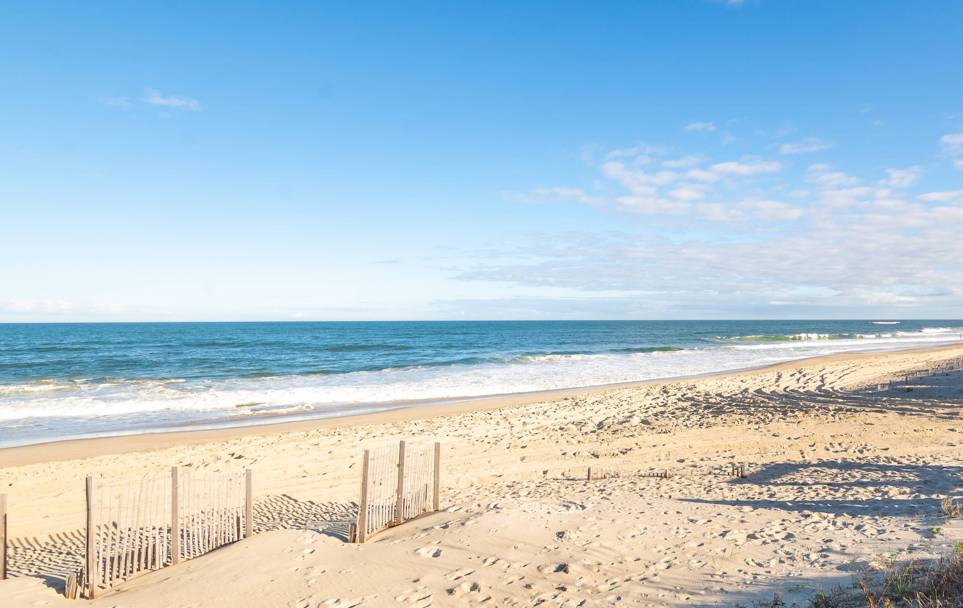 Een zandstrand met een houten omheining en golven.