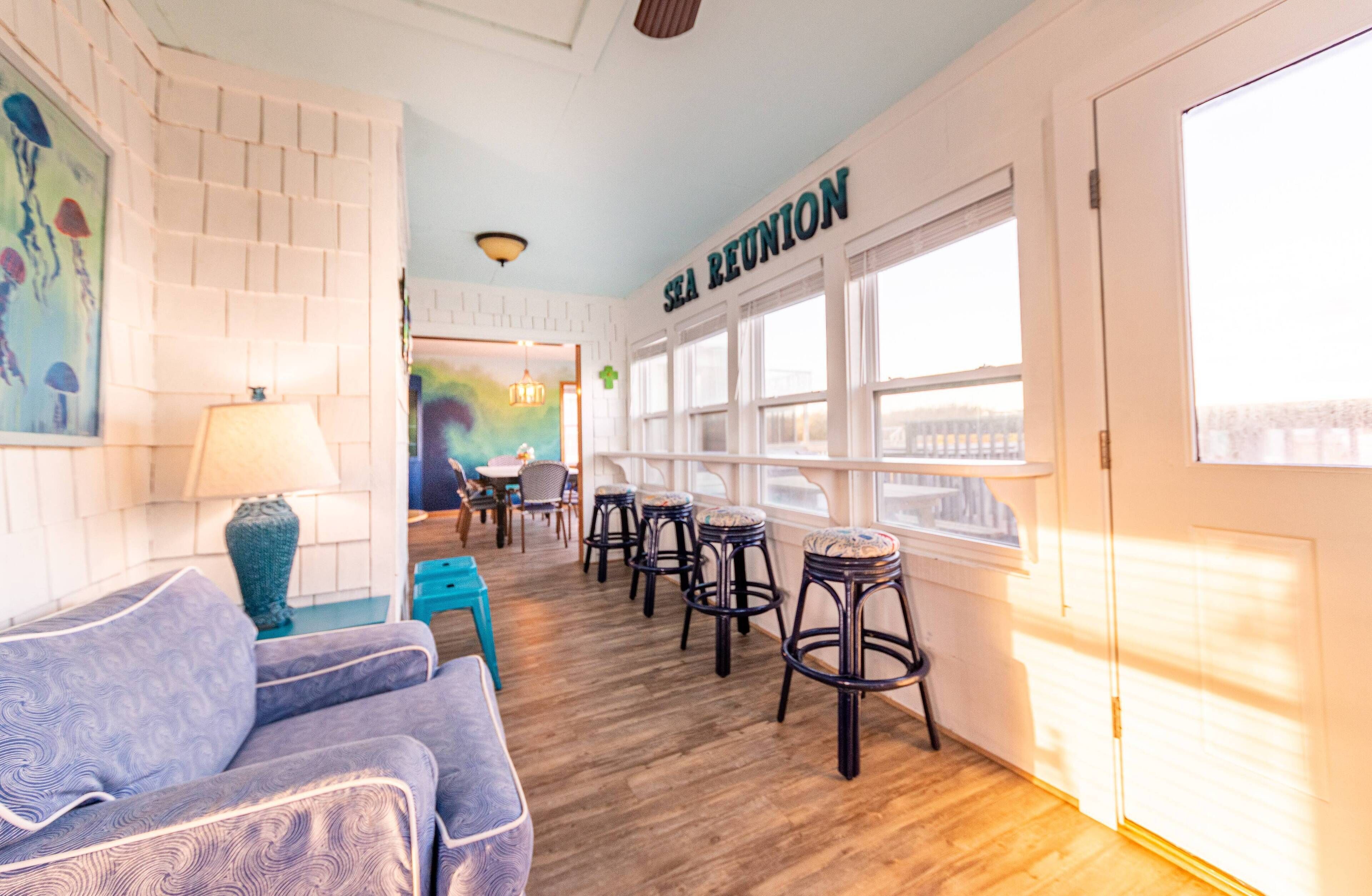 A room with a blue sofa, a table with chairs, a bar area with stools, and a large window with a view.
