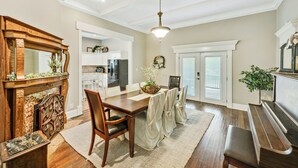 Un coin repas avec une table en bois, des chaises et un banc. On y trouve une cheminée agrémentée d’un miroir et d’une plante posée sur le manteau.