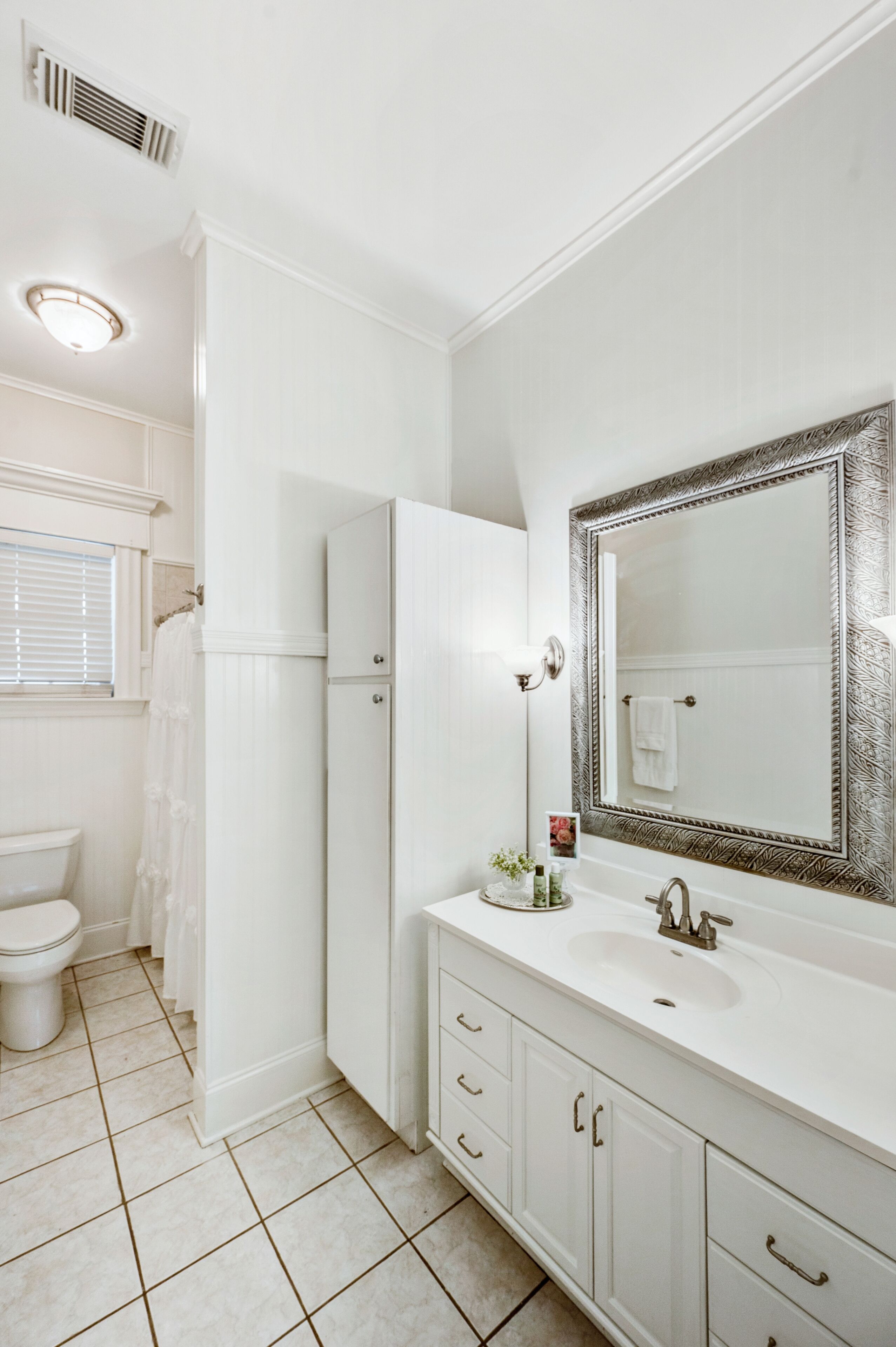 Une salle de bain avec des éléments d’aménagement blancs, un grand miroir et des toilettes.
