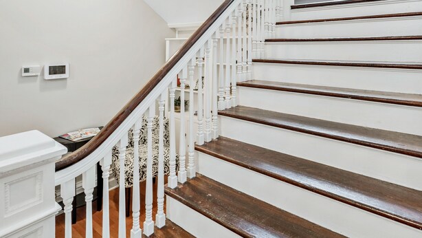 Un magnifique escalier avec des rampes blanches et des marches en bois, menant à un palier doté d’une grande fenêtre en arc de cercle.