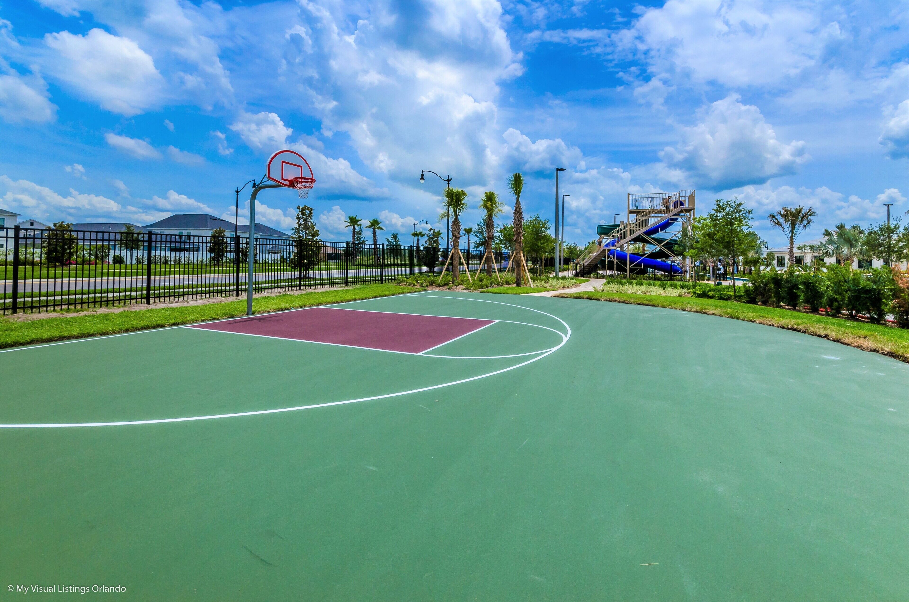 Una cancha de baloncesto al aire libre con superficie verde, un área clave roja y un aro de baloncesto.