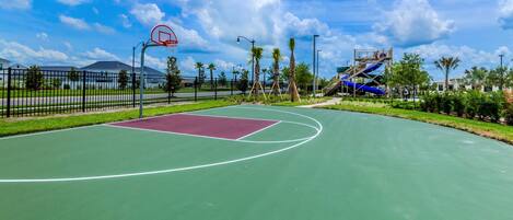 Una cancha de baloncesto al aire libre con superficie verde, un área clave roja y un aro de baloncesto.