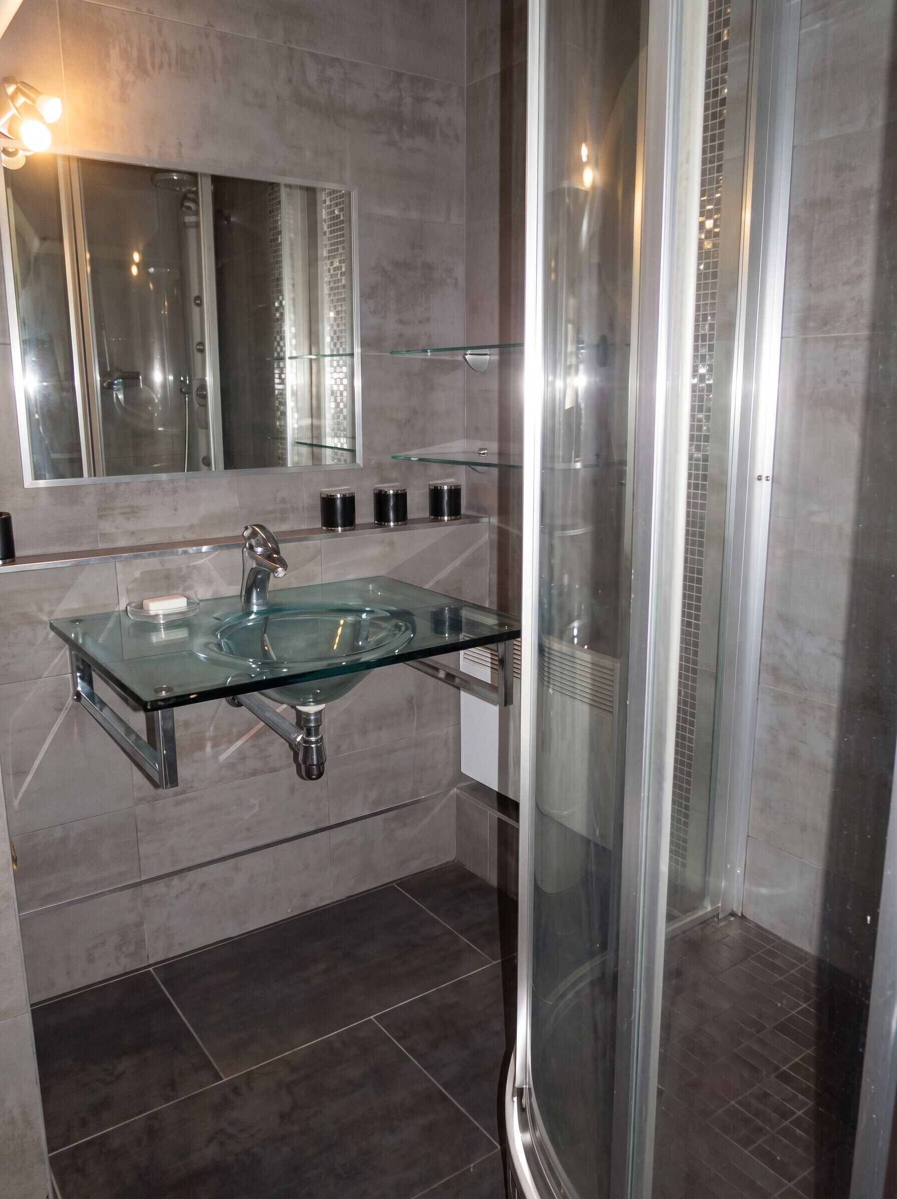 Un bagno moderno con un lavandino in vetro, uno spazio doccia e uno specchio grande.