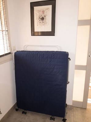 A room with a bed, a window with blinds, a framed artwork on the wall, and a door.