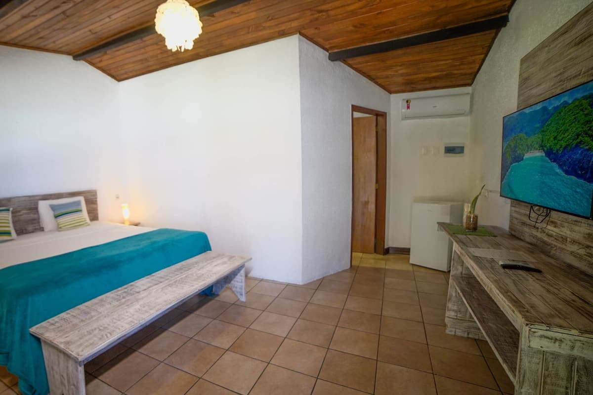 A bedroom with a bed, bench, wooden ceiling, white walls, and a TV on the wall.