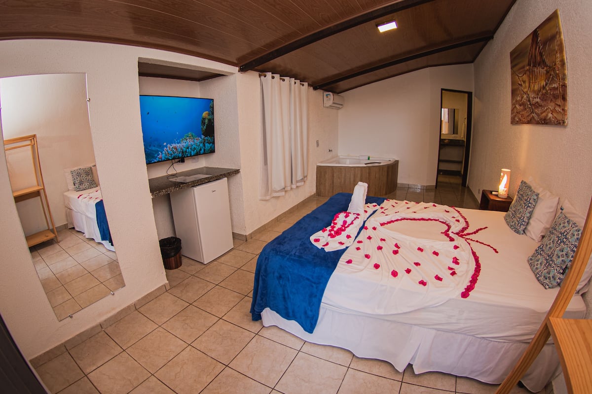 A bedroom with a bed, a TV, a bathroom, and a shower area.
