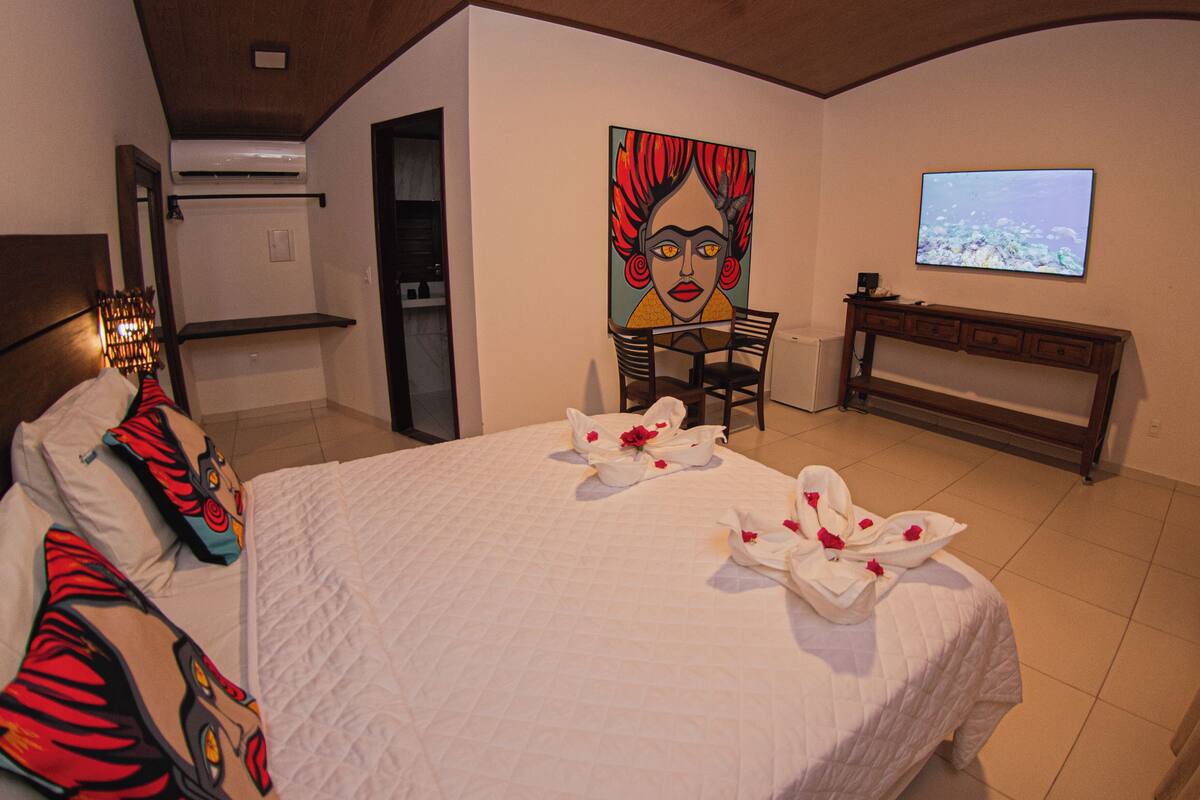 A hotel room with a bed, a painting, a TV, and a desk.