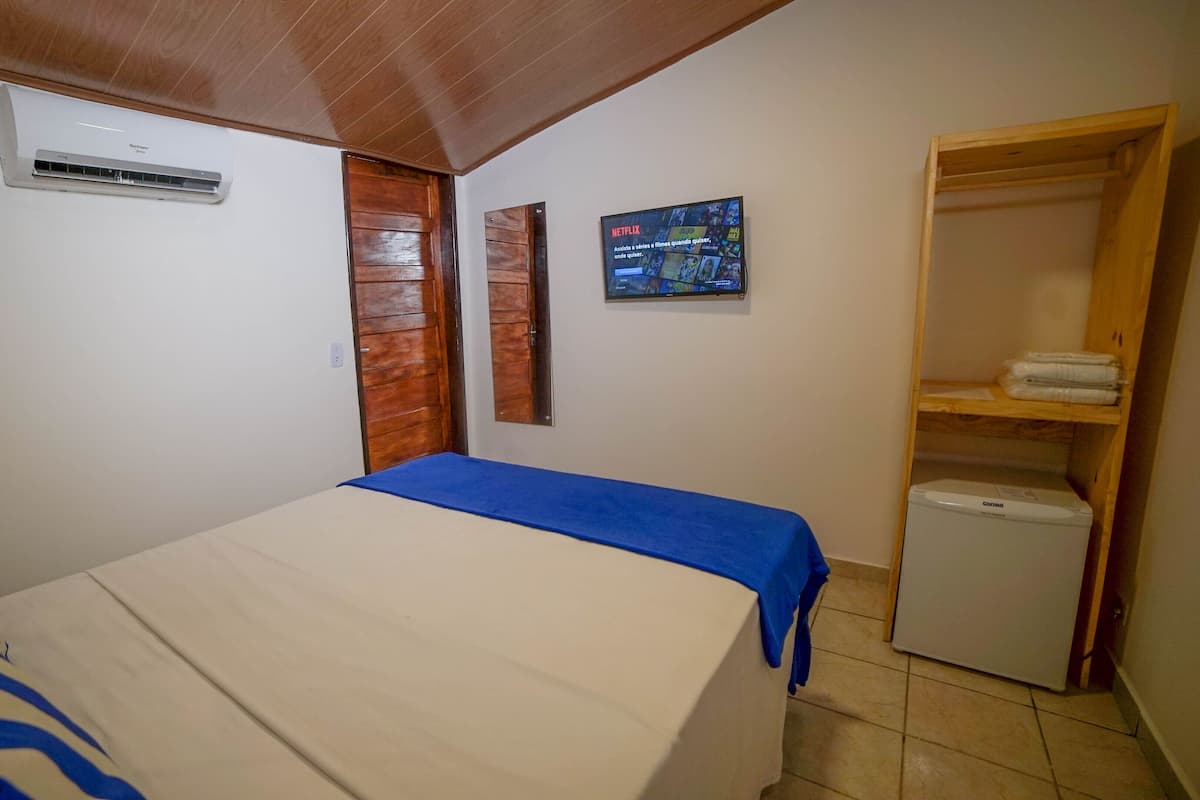 A bedroom with a bed, a wardrobe, a small table, and an air conditioning unit.