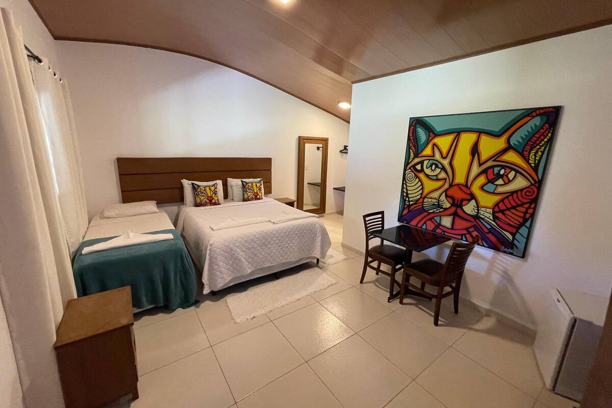 A bedroom with two beds, a desk, and a colorful cat painting on the wall.
