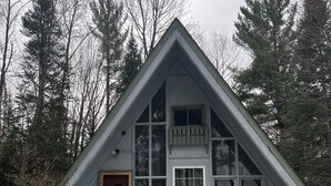 A cabin with a steeply pitched roof, a front porch with a white picket railing, and a small set of stairs leading to the entrance.