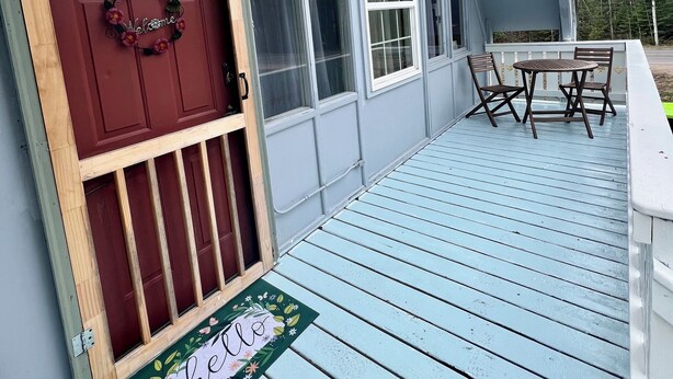 A house with a red door, a 'welcome' sign, and a deck with chairs.