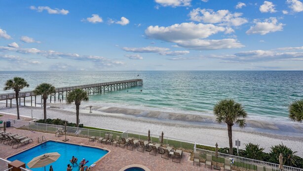 A beach view with a pool, palm trees, and a pier.