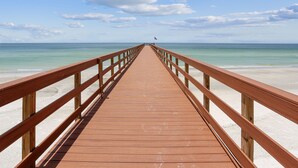 A wooden pier leading to a beach with clear skies and calm waters.