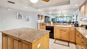 A modern kitchen with granite countertops, wooden cabinets, a ceiling fan, and recessed lighting.