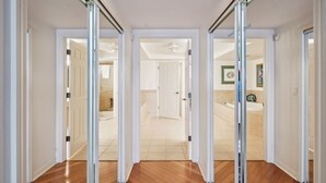 A hallway with glass doors leading to a bathroom with a bathtub and a shower.