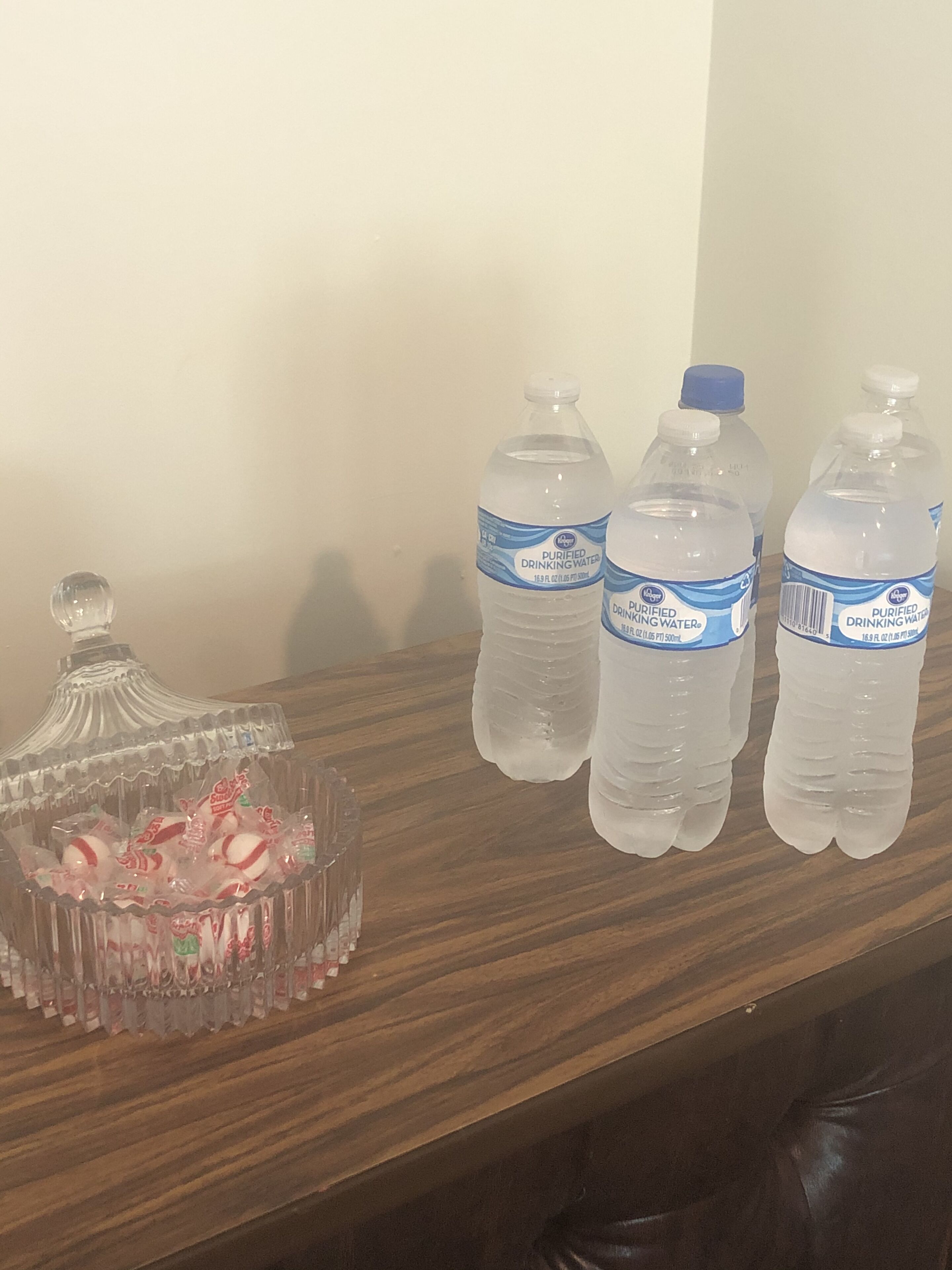 A wooden table with three bottles of purified drinking water and a glass container with candies.