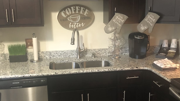 Een keuken met donkere kastjes, een granieten aanrecht, een bord met opschrift ‘koffie’ en een koffiezetapparaat.