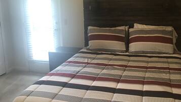 Un dormitorio con cama, mesita de noche, decoración en la pared y ventana con persianas.