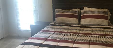 A bedroom with a bed, a nightstand, a wall decoration, and a window with blinds.