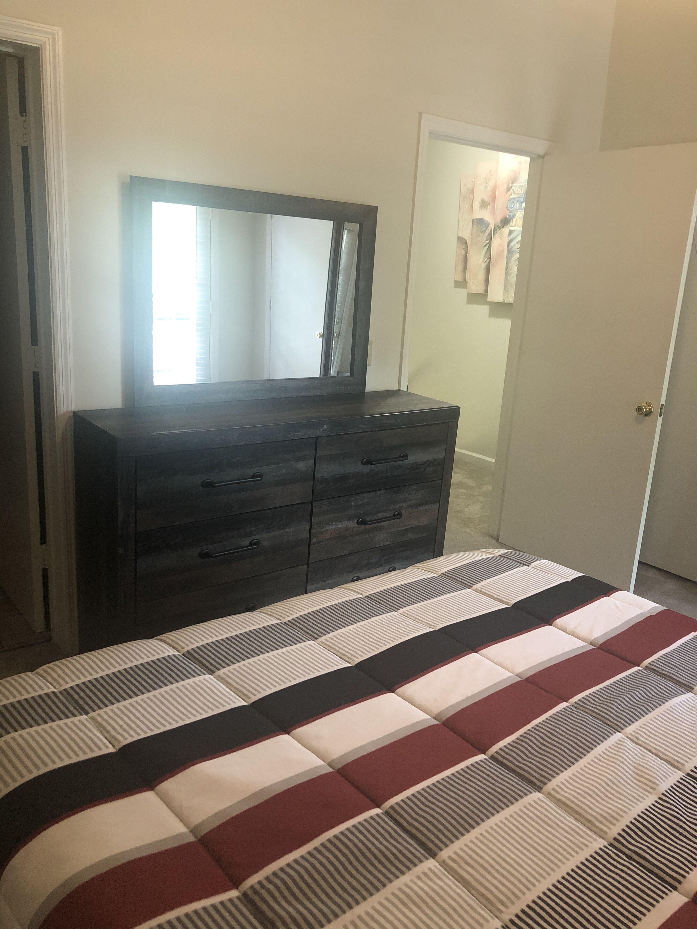 Un dormitorio con un aparador de madera oscura, un espejo grande y una cama con colcha a rayas.